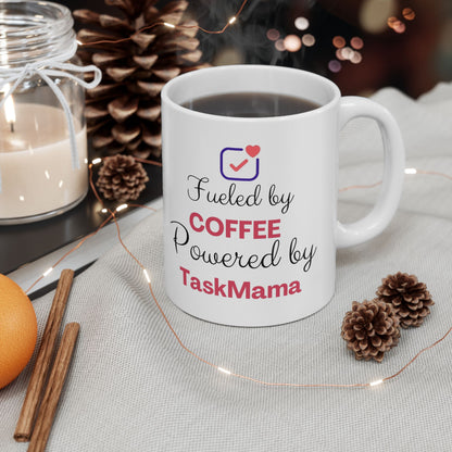 White mug with 'Fueled by COFFEE Powered by TaskMama' text, surrounded by decorative items on a table.