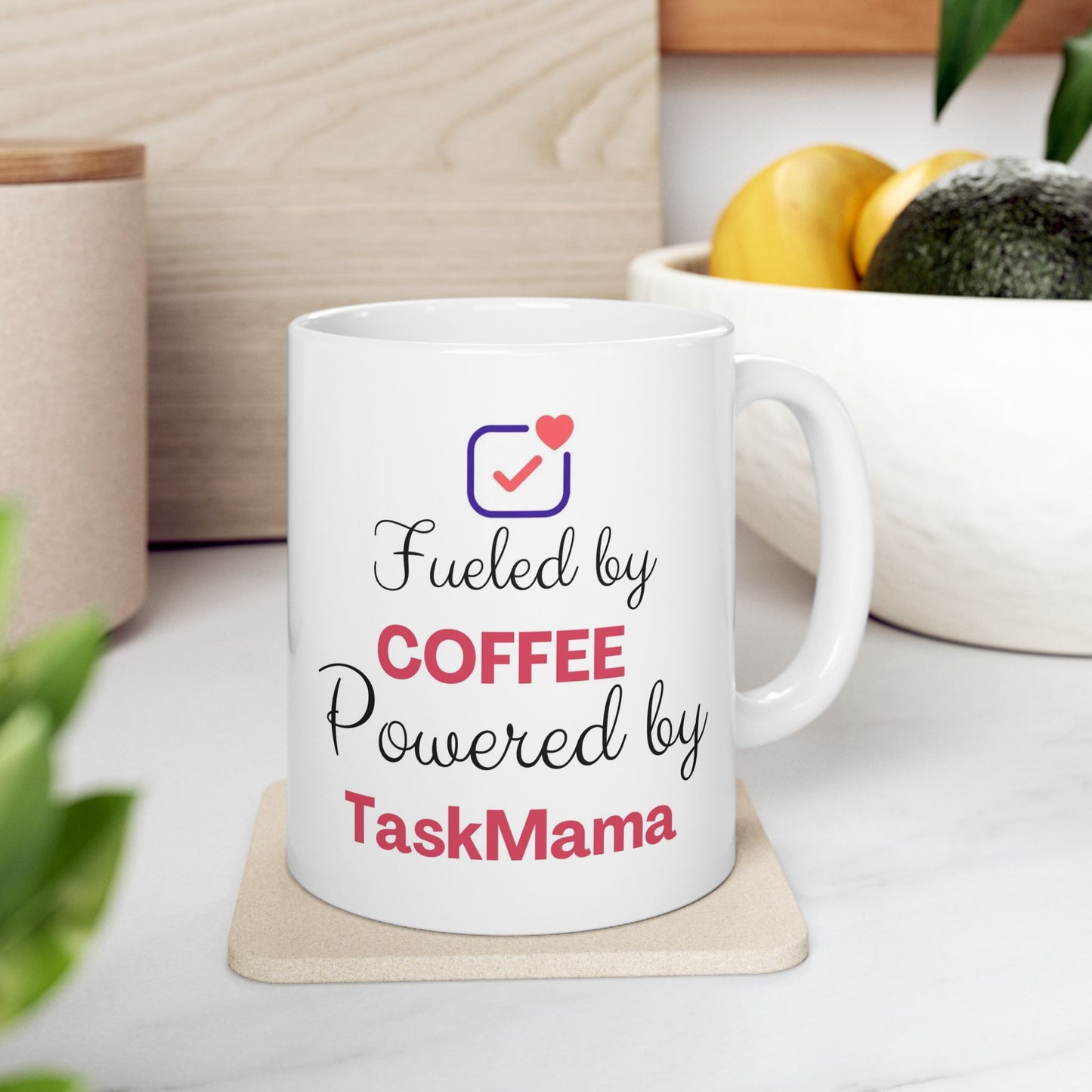 White mug with text 'Fueled by Coffee, Powered by TaskMama' on a coaster.