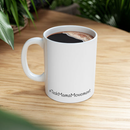 White mug with 'TaskMamaMovement' text on a wooden table with coffee.