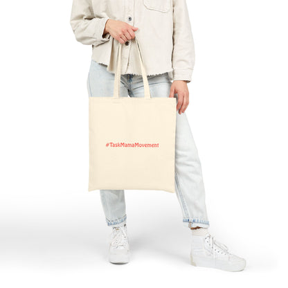 Person holding a beige tote bag with '#TaskMamaMovement' text on a white background